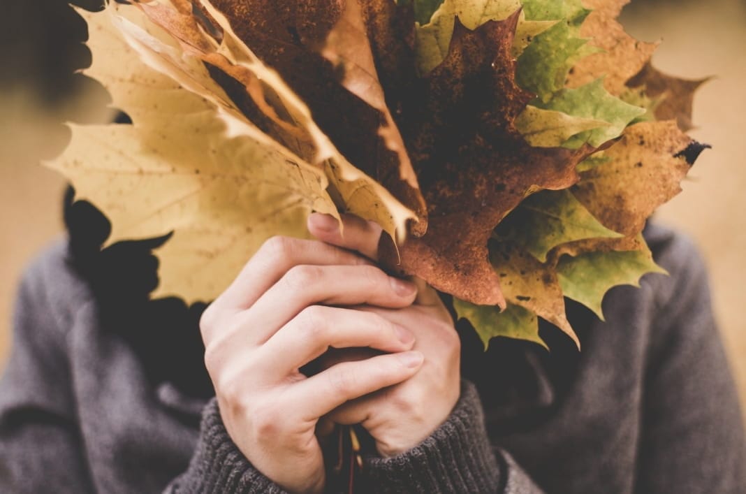 Vrouw verbergt haar gezicht achter herfstbladeren