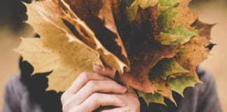 Vrouw verbergt haar gezicht achter herfstbladeren